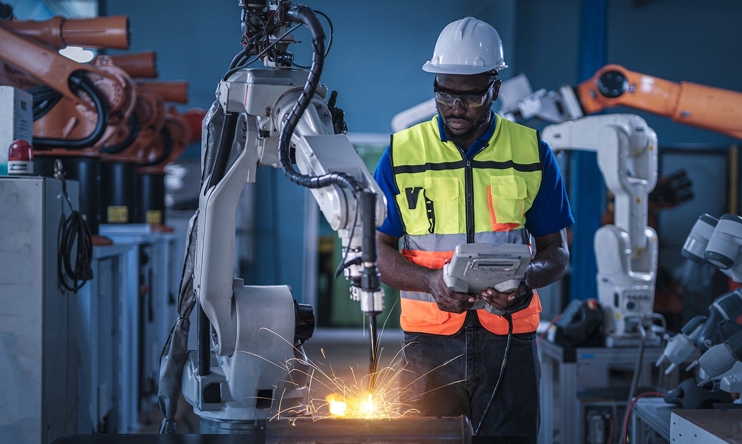 Engineers in safety equipment controlling a welding robotic arm
